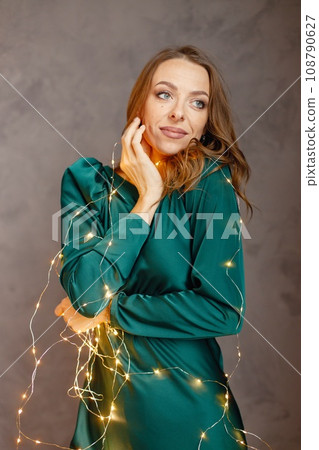 Portrait of a young woman celebrating Christmas Eve. Model posing for a photo. Woman wearing green dress. 108790627