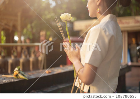 A beautiful Thai woman is making a wish and paying respect to the image of the Buddha at a temple. 108790653