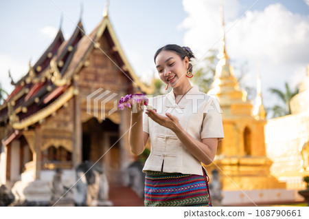 A charming Thai woman in a traditional Thai-Lanna dress is admiring a beautiful garland in her hand. A charming Thai woman in a traditional Thai-Lanna dress is admiring a beautiful garland in her hand. 108790661