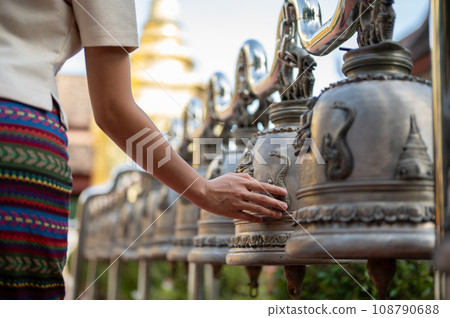 Close-up image of an Asian woman in a traditional Thai dress is ringing temple bells in a temple. 108790688