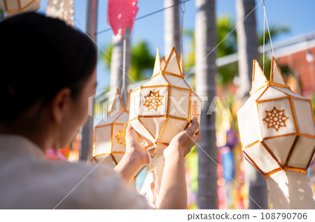 A beautiful Thai-Asian woman is hanging a paper lantern and enjoying YI Peng festival at a temple. A beautiful Thai-Asian woman is hanging a paper lantern and enjoying YI Peng festival at a temple. 108790706