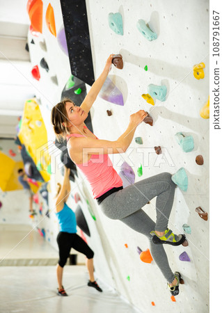 Young female alpinist practicing indoor rock-climbing on a artificial boulder without safety belts 108791667