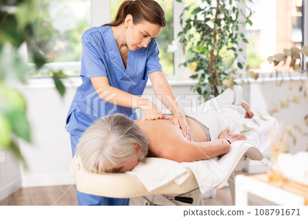 Skilled young masseuse doing back pain relief massage to elderly woman 108791671