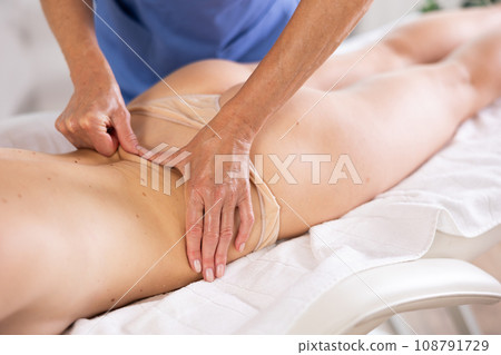 Masseuse hands doing back pain relief massage to young woman Masseuse hands doing back pain relief massage to young woman 108791729