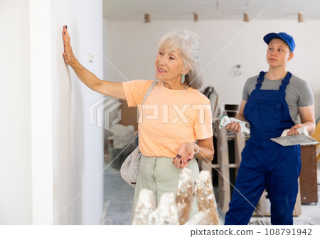 Senior woman evaluating quality of teenager boy's work in construciton site Senior woman evaluating quality of teenager boy's work in construciton site 108791942