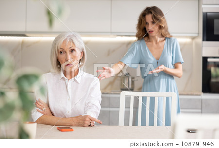 Adult woman quarreling with elderly woman in kitchen Adult woman quarreling with elderly woman in kitchen 108791946