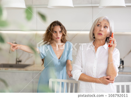 Adult woman quarreling with elderly woman talking on phone Adult woman quarreling with elderly woman talking on phone 108792011