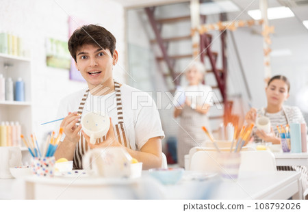 Cheerful skilled young artist painting ceramic cup in pottery workshop 108792026