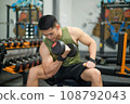 lifting a dumbbell to work the muscles in his bicep. 108792043