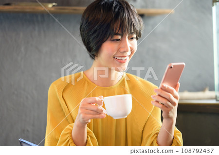 A woman looking at her smartphone while drinking coffee at a cafe. Photographed in cooperation with "Western confectionery shop sentiment" 108792437
