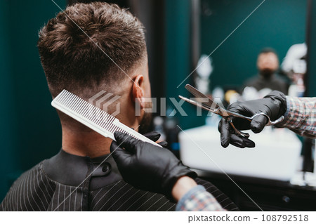 Man in barbershop, close-up hairdresser making haircut to bearded male Man in barbershop, close-up hairdresser making haircut to bearded male 108792518