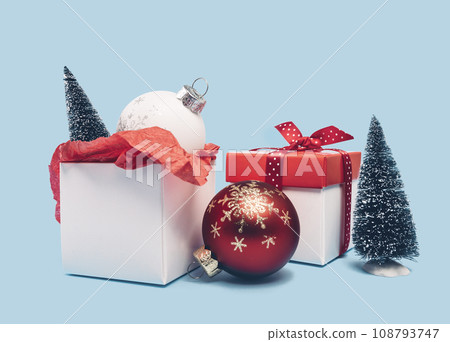 Two red and white gift boxes and ornaments with Christmas trees on baby blue background. Assorted size. Merry Christmas and Happy New Year gift shopping and sale concept Two red and white gift boxes and ornaments with Christmas trees on baby blue background. Assorted size. Merry Christmas and Happy New Year gift shopping and sale concept 108793747