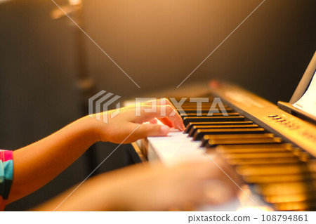 Close-up of a little student's hand playing the piano. Happy young Asian girl learning and practicing the piano. Selective focus. Close-up of a little student's hand playing the piano. Happy young Asian girl learning and practicing the piano. Selective focus. 108794861