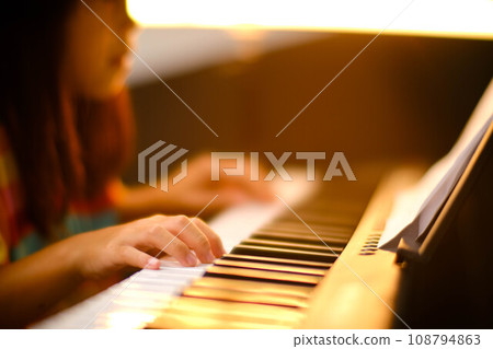 Close-up of a little student's hand playing the piano. Happy young Asian girl learning and practicing the piano. Selective focus. Close-up of a little student's hand playing the piano. Happy young Asian girl learning and practicing the piano. Selective focus. 108794863