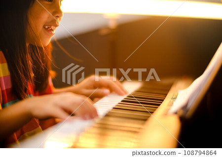 Close-up of a little student's hand playing the piano. Happy young Asian girl learning and practicing the piano. Selective focus. Close-up of a little student's hand playing the piano. Happy young Asian girl learning and practicing the piano. Selective focus. 108794864