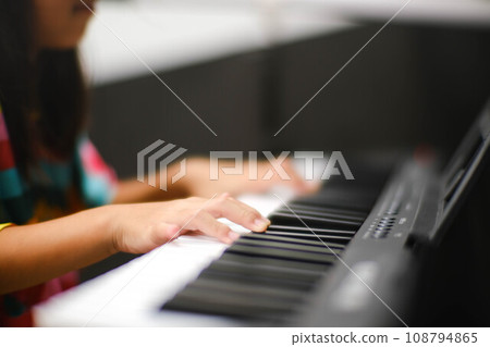 Close-up of a little student's hand playing the piano. Happy young Asian girl learning and practicing the piano. Selective focus. Close-up of a little student's hand playing the piano. Happy young Asian girl learning and practicing the piano. Selective focus. 108794865