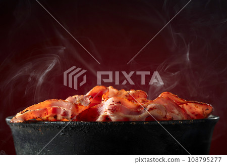 Fried steaming bacon slices in an old black pan. 108795277
