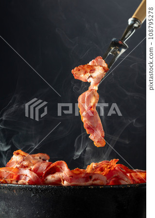 Fried steaming bacon slices on a black background. Fried steaming bacon slices on a black background. 108795278