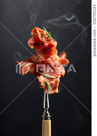 Roasted bacon slices with rosemary on a fork. 108795283