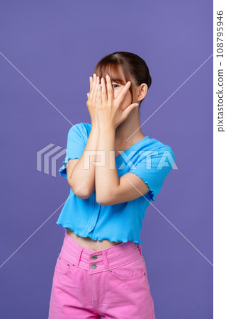 Young woman covering face with hands, looking through fingers, peeking with curiosity at something Young woman covering face with hands, looking through fingers, peeking with curiosity at something 108795946