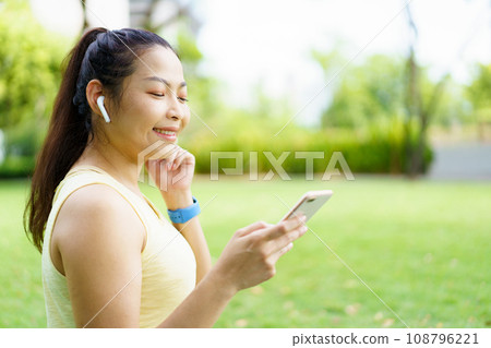 Healthy happy Asian woman enjoy running exercise at the park and listening music on wireless headphone while running. Beautiful Asian woman listening music on an earphones while running. Healthy happy Asian woman enjoy running exercise at the park and listening music on wireless headphone while running. Beautiful Asian woman listening music on an earphones while running. 108796221