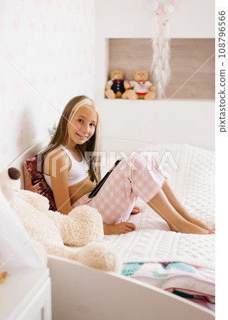 Girl with a tablet computer on the bed in the bedroom in the morning. A teenager texts and plays an online game. Schoolboy posting on social media, doing homework for distance learning, video chatting 108796566