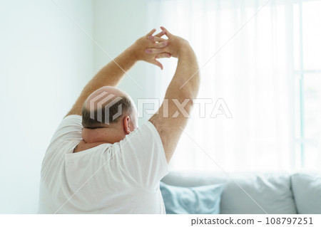 Caucasian white man wake up from the bed in morning and sitting beside the bed then doing a stretch oneself. A cozy lazy overweight fat man sitting on the bed after woke up in morning. 108797251