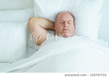 Caucasian white oversize body - fat man sleeping on the bed in bedroom close up. Health care and wellbeing concept. Caucasian white oversize body - fat man sleeping on the bed in bedroom close up. Health care and wellbeing concept. 108797258