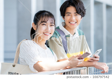 Young male and female university students holding smartphones and talking Young male and female university students holding smartphones and talking 108797542