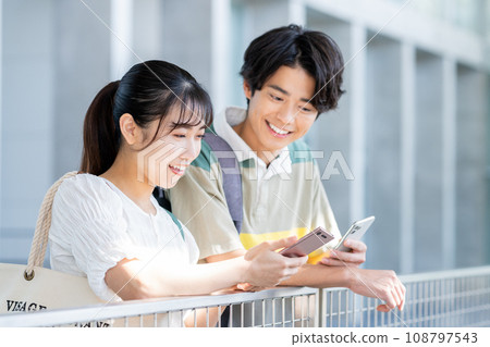 Young male and female university students holding smartphones and talking Young male and female university students holding smartphones and talking 108797543