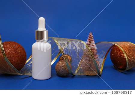 Cosmetic product oil or face serum on blue christmas background with golden decorations. Winter skin care 108798517