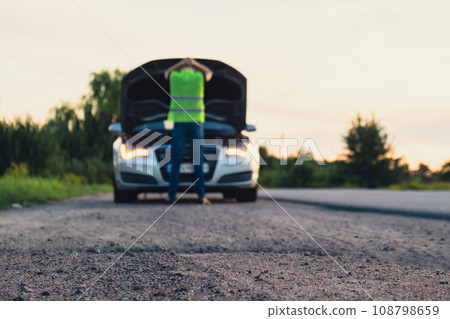 Broken silver luxury car emergency accident. Man driver installing red triangle stop sign on road. Sport automobile turned on blinkers technical problems on the road. Safety procedure vehicle broken 108798659