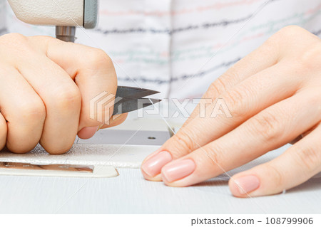 Female hands of a master tailor cuts a thread with scissors Female hands of a master tailor cuts a thread with scissors 108799906