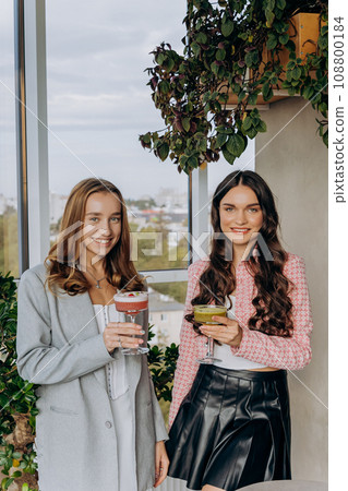 Attractive women are clinking and toasting with cocktails in restaurant or bar while looks camera Attractive women are clinking and toasting with cocktails in restaurant or bar while looks camera 108800184