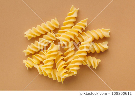Uncooked fusilli pasta. Uncooked italian pasta on brown background. Top view. 108800611