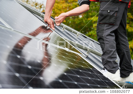 Man mounter mounting photovoltaic solar panels on roof of house. Close up view of engineer installing solar module system with help of hex key. Concept of alternative, renewable energy. 108802077