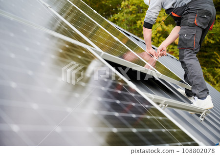 Man technician mounting photovoltaic solar panels on roof of house. Close up view of engineer installing solar module system with help of hex key. Concept of alternative, renewable energy. 108802078