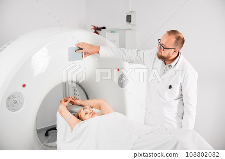 Medical computed tomography or MRI scanner. Male radiologist presses MRI button to examine female patient. Concept of healthcare and modern diagnostics. Medical computed tomography or MRI scanner. Male radiologist presses MRI button to examine female patient. Concept of healthcare and modern diagnostics. 108802082