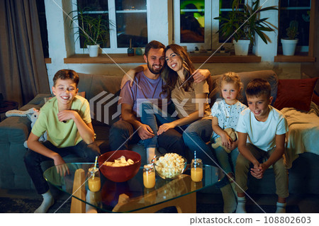 Happy, loving parents hugging, sitting on couch with children in evening and watching tv. Lovely family time Happy, loving parents hugging, sitting on couch with children in evening and watching tv. Lovely family time 108802603