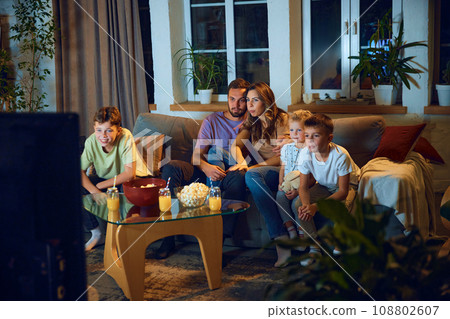 Hugging man and woman, parents sitting on couch with their children and watching tv in the evening. Family time 108802607