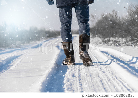 A traveler in boots walks along a snowy winter road 108802853