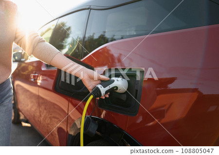 Woman holds plug of electric car charging station. 108805047