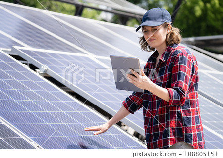 Woman with digital tablet stands next to solar panel Woman with digital tablet stands next to solar panel 108805151