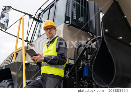 Engineer with tablet computer stands on the stairs to the cab of a truck. Engineer with tablet computer stands on the stairs to the cab of a truck. 108805334