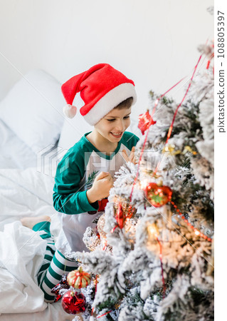 Close up of caucasian child hands putting ornaments on Christmas tree style in gold and white. Generation alpha and gen alpha children. Close up of caucasian child hands putting ornaments on Christmas tree style in gold and white. Generation alpha and gen alpha children. 108805397