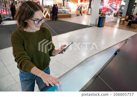 Woman with phone uses self-service kiosk in the shopping mall 108805757