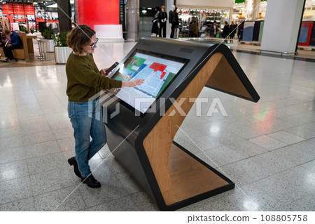 Woman with phone uses self-service kiosk in the shopping mall Woman with phone uses self-service kiosk in the shopping mall 108805758