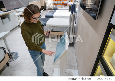Woman with phone uses self-service kiosk in the shopping mall 108805759