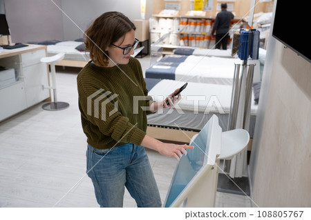 Woman with phone uses self-service kiosk in the shopping mall 108805767