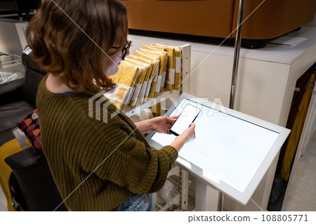 Woman with phone uses self-service kiosk in the shopping mall 108805771